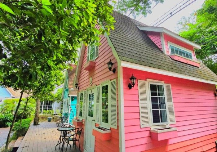 A pink house with white trim and shutters is surrounded by trees.