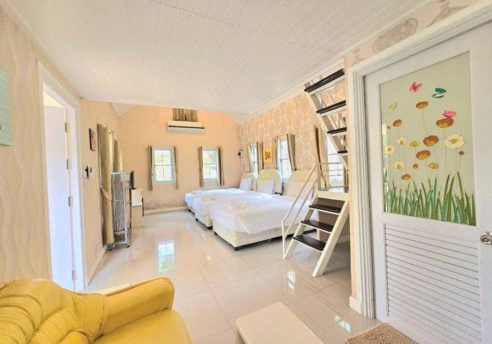 A hotel room with two beds , a yellow couch , and stairs leading up to the second floor.