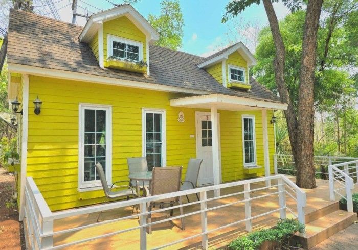 A small yellow house with a porch and a table and chairs on it.