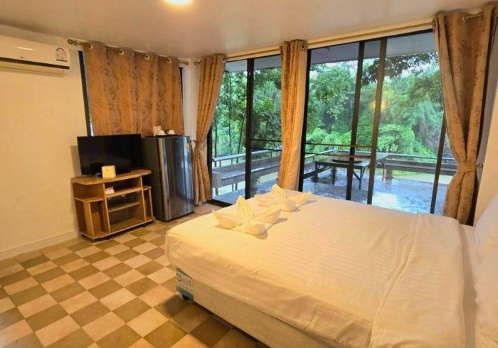 A bedroom with a bed , television , refrigerator and sliding glass doors.