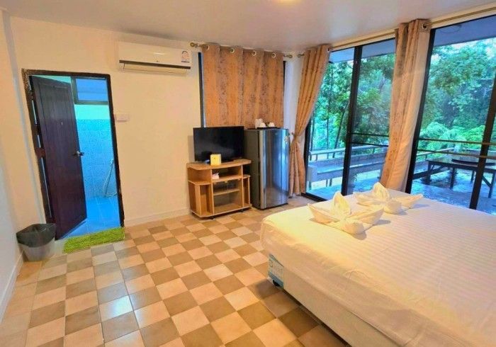 A bedroom with a bed , television , refrigerator and a balcony.