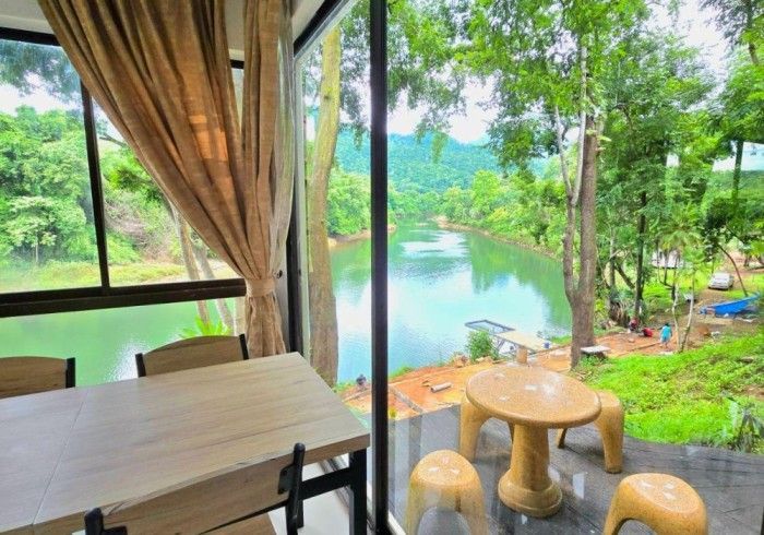 There is a table and chairs in the room with a view of a lake.