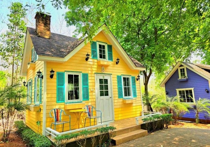 A yellow house with blue shutters is next to a blue house.