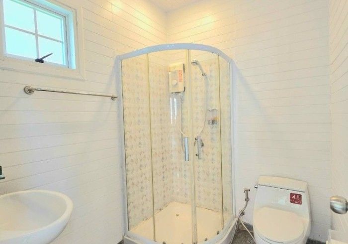 A bathroom with a shower , toilet , sink and window.