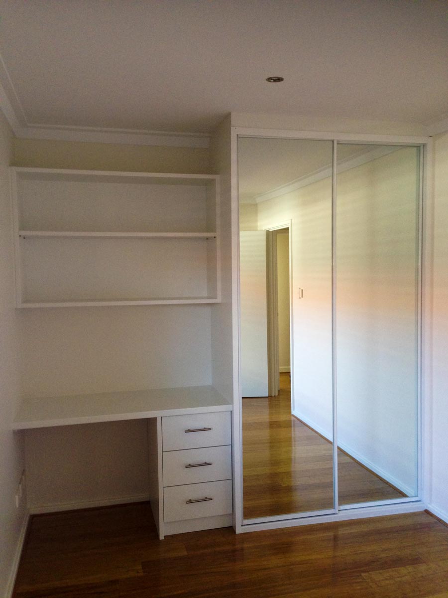 mirrored sliding wardrobe with white frame and desk to the left side