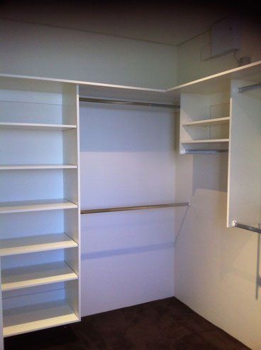 corner of white shelved and silver rod walk in wardrobe
