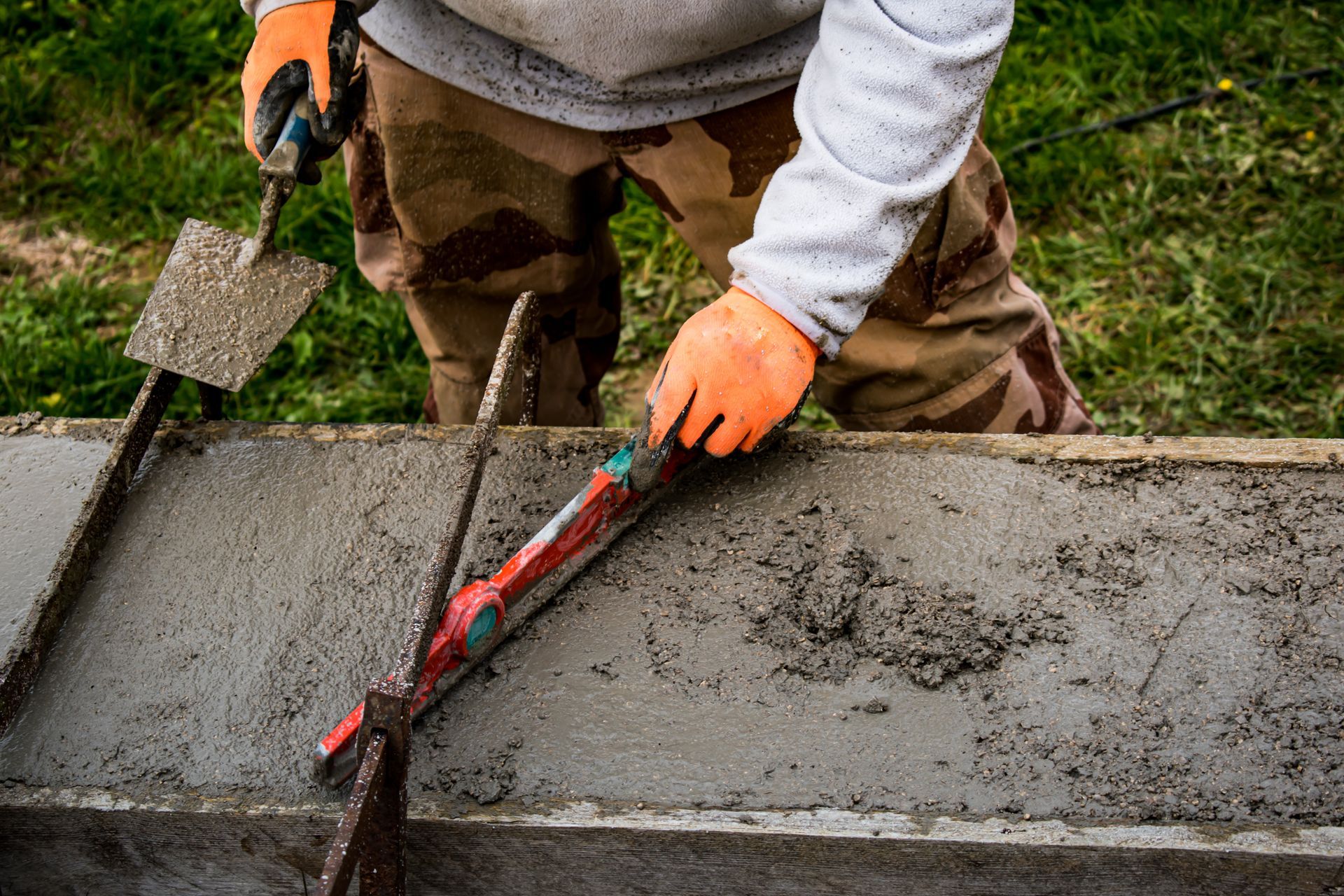 A man is working on a concrete wall with a shovel and level.