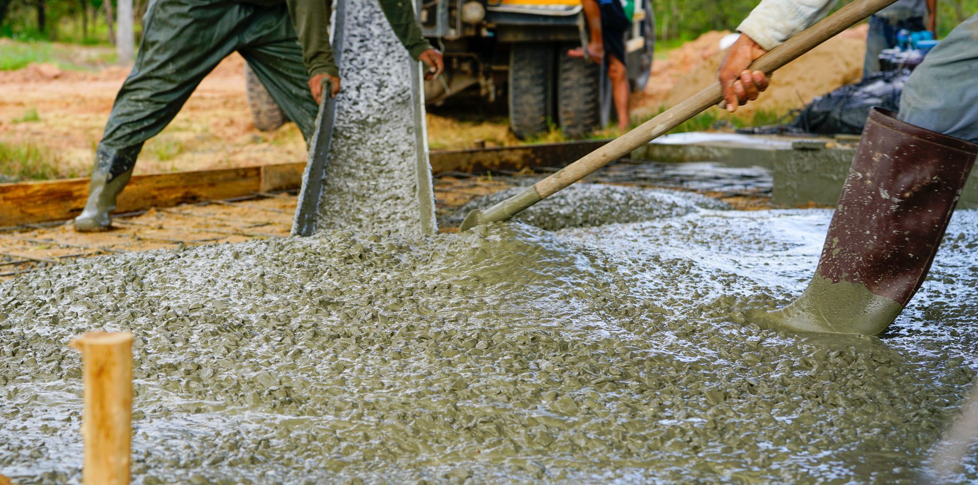 A man is pouring concrete into a hole with a shovel.
