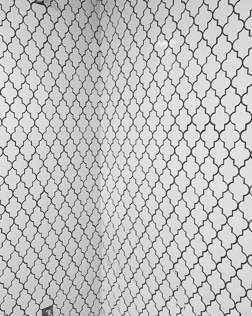 A close up of a white tile wall with a black pattern.