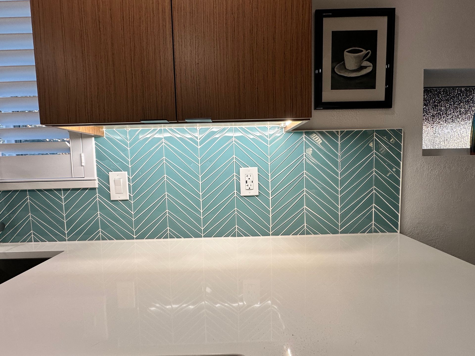 There is a picture of a cup of coffee on the wall above the counter in the kitchen.