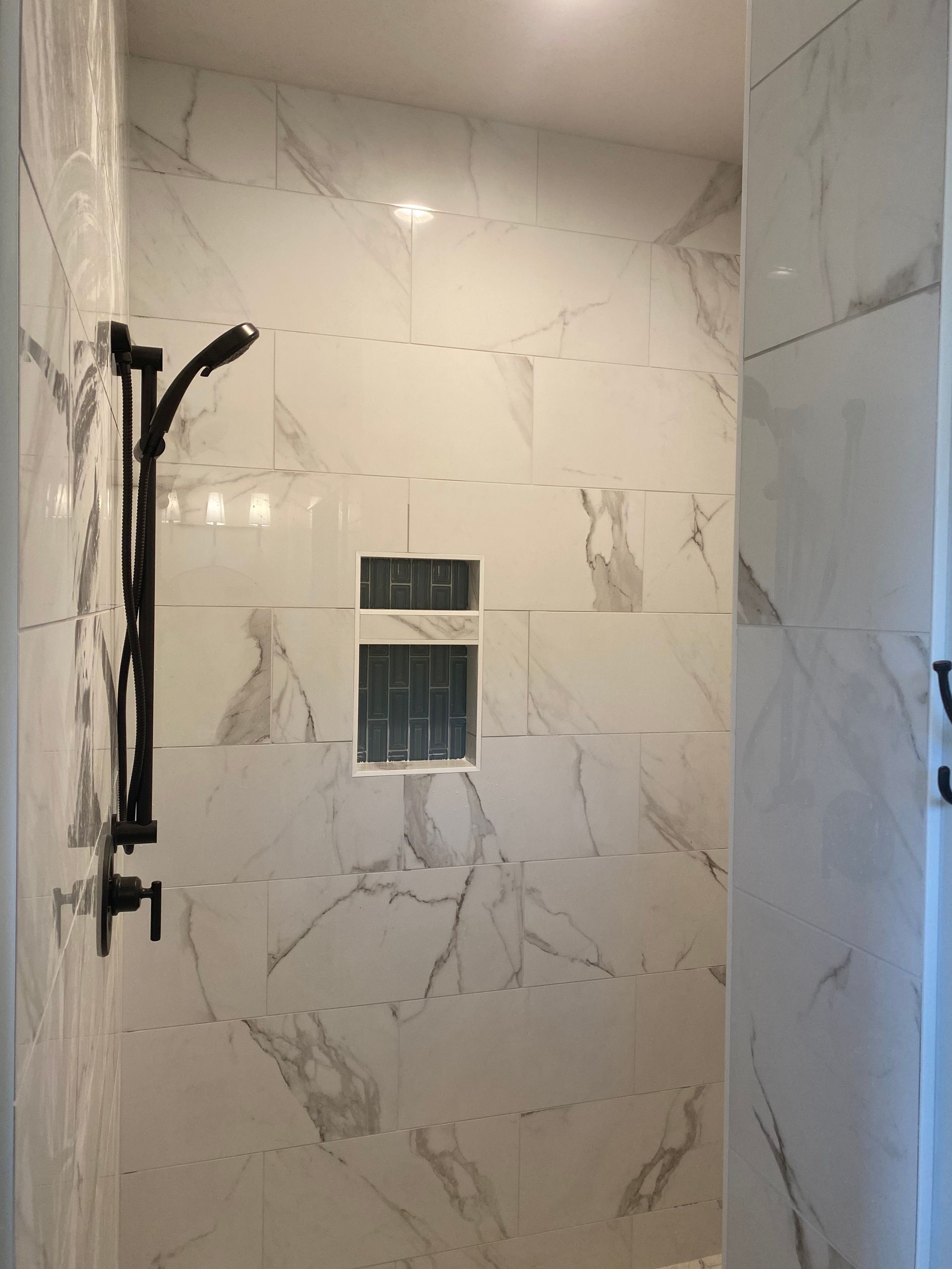 A shower with white tiles and a black shower head.