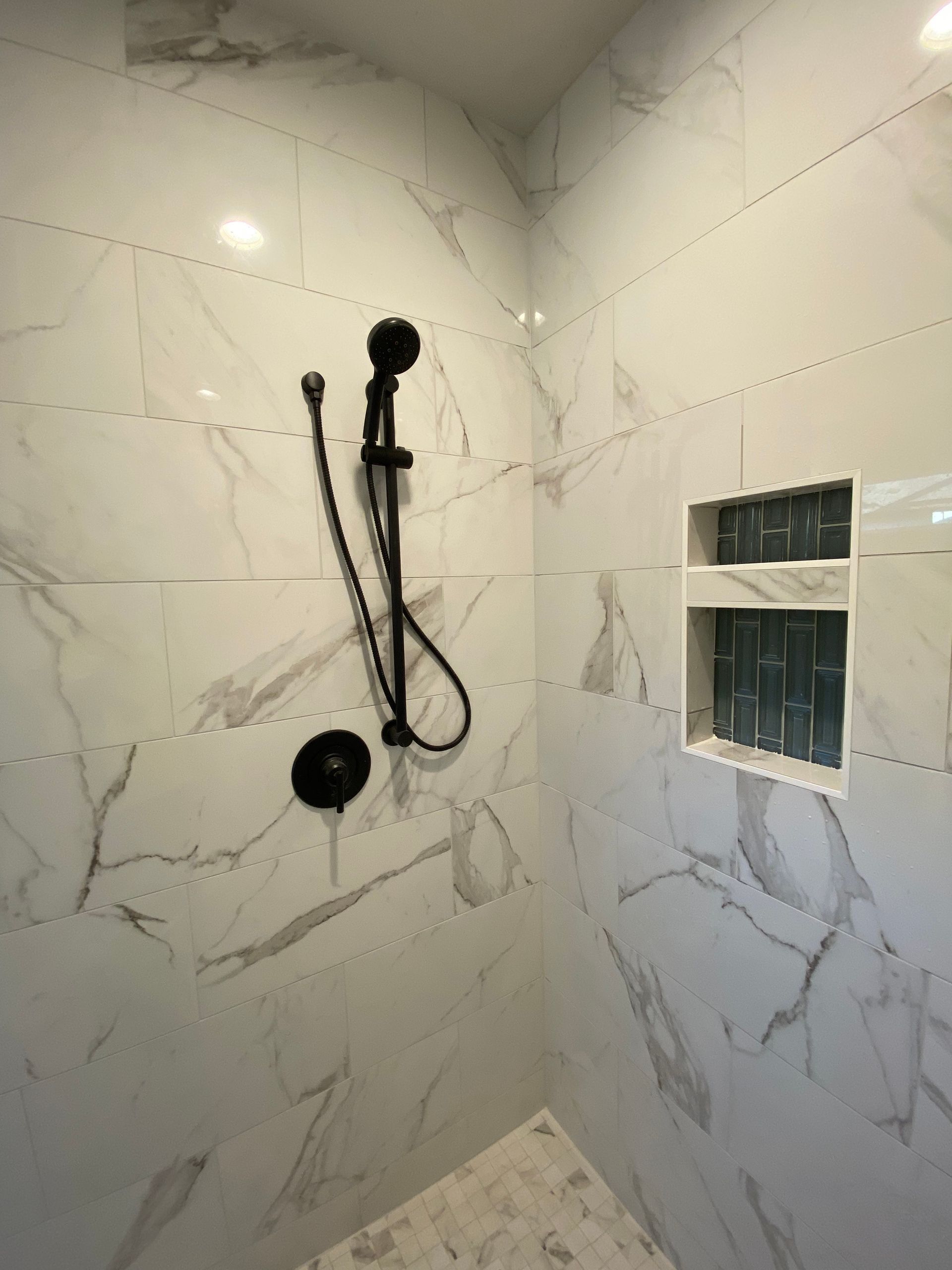 A shower with marble tiles and a black shower head.