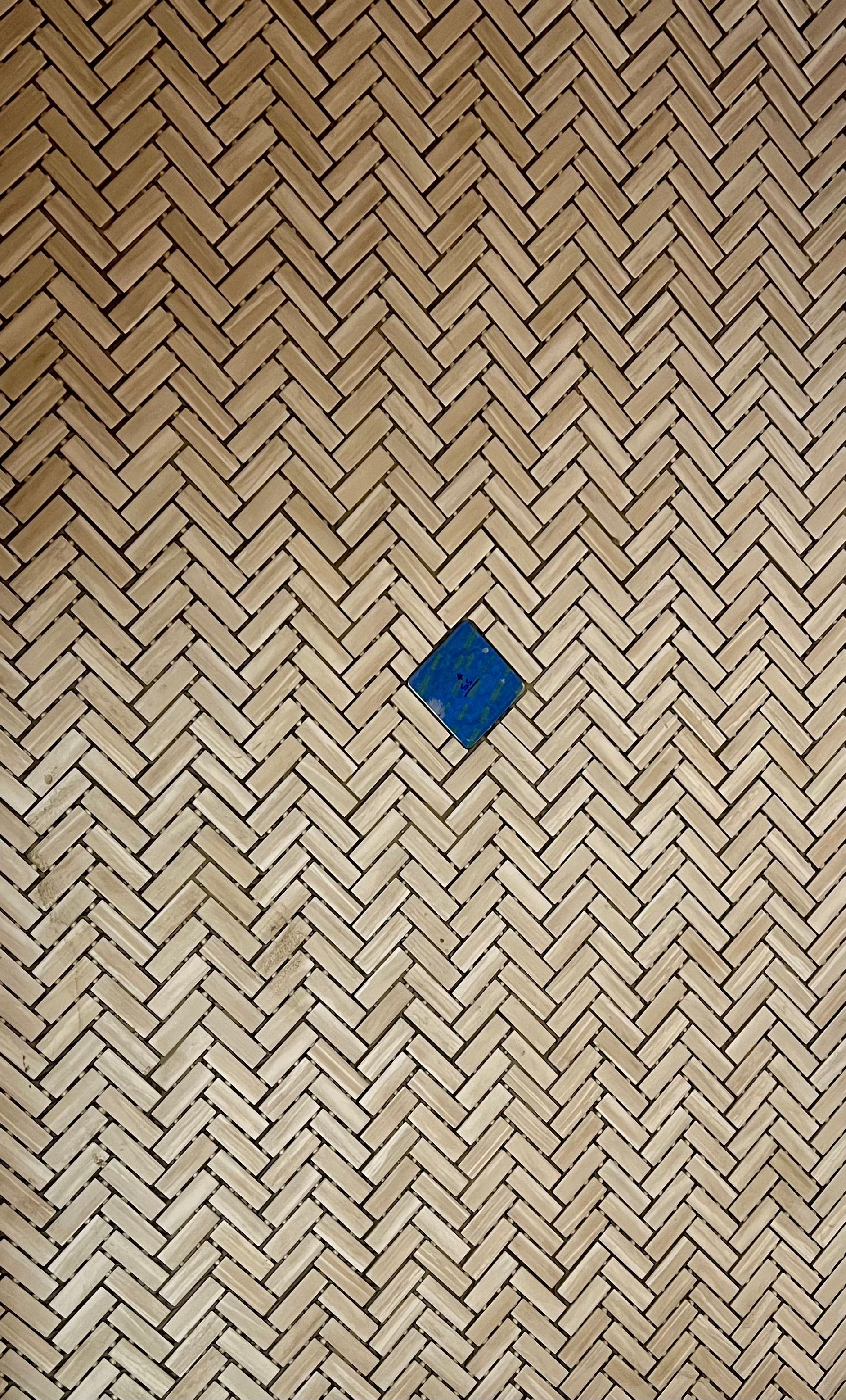 A close up of a herringbone tile floor with a blue square in the middle.