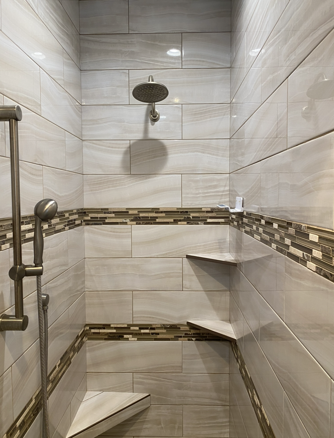 There is a shower with a shower head and shelves.