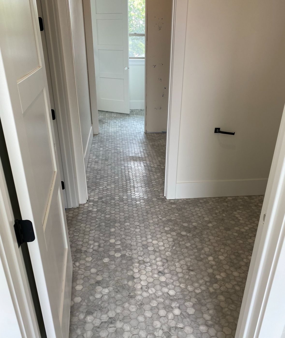 A hallway with white tile floors and white doors leading to a bathroom.
