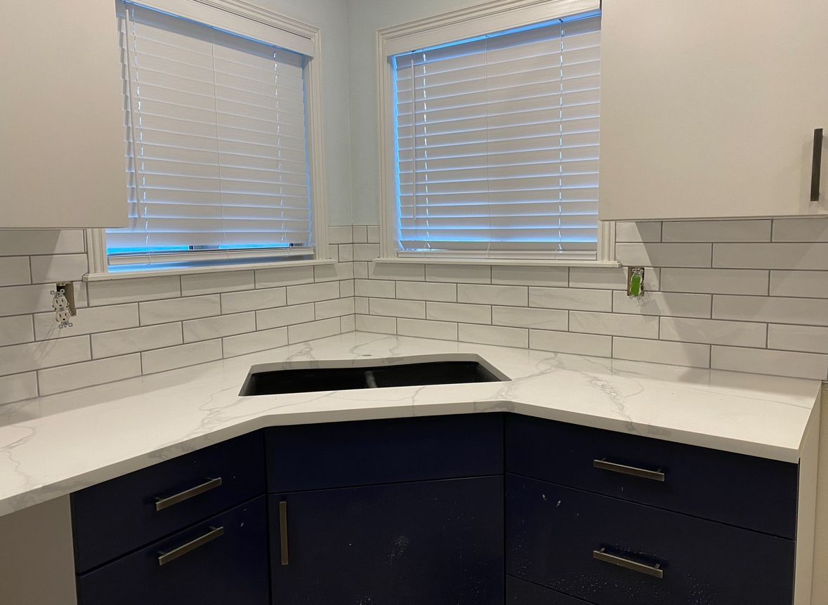 A kitchen with blue cabinets , white counter tops , and a sink.
