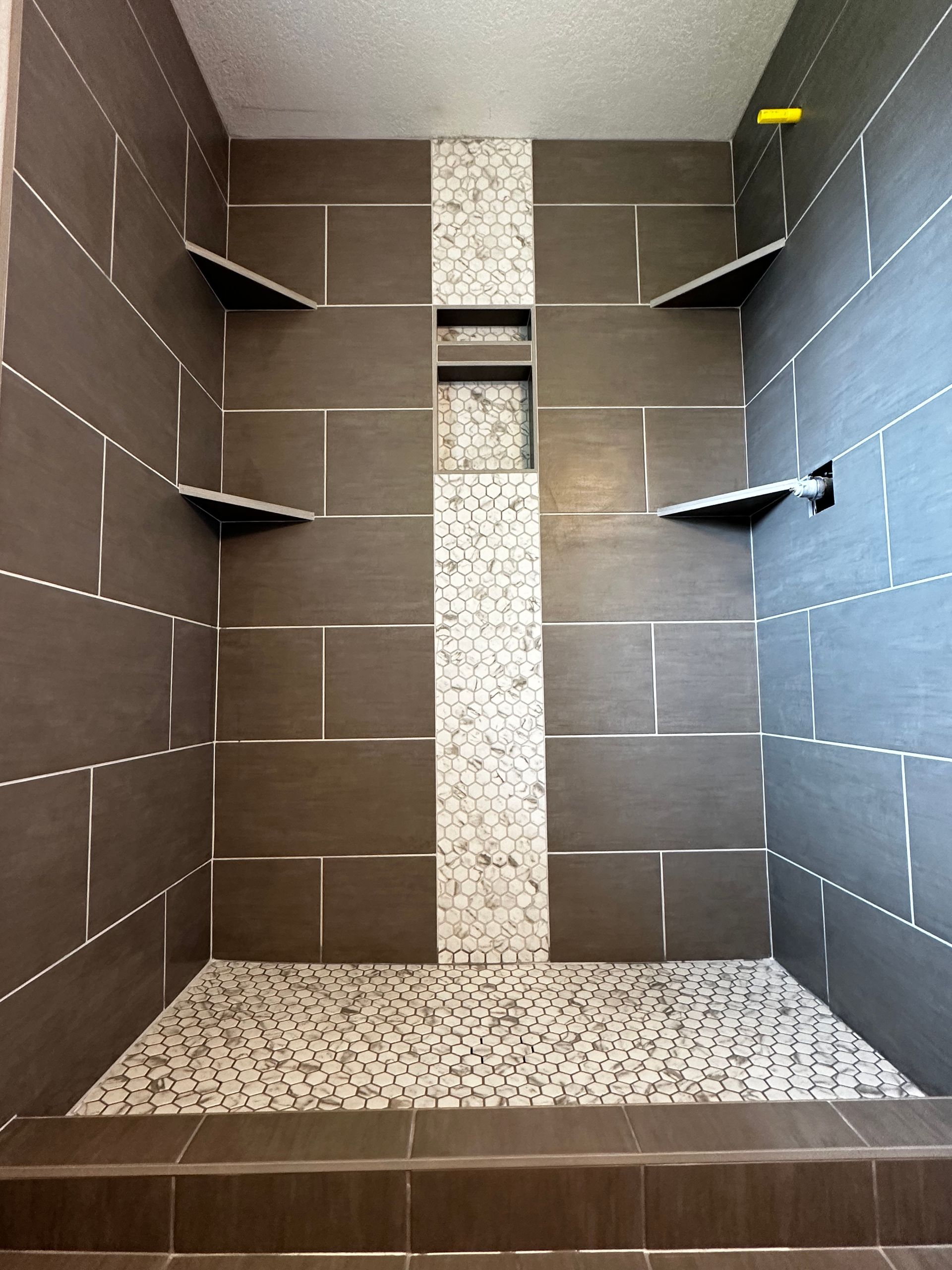 A walk in shower with brown and white tiles and shelves