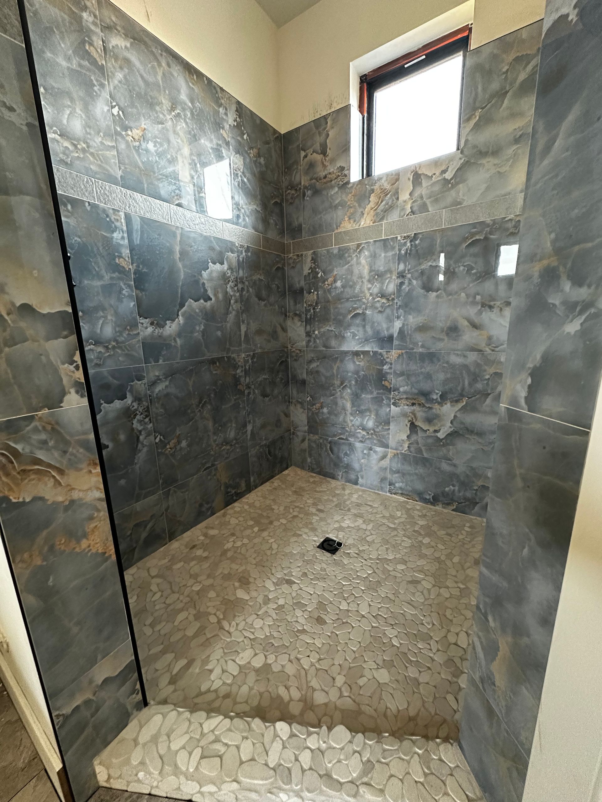 A bathroom with a walk in shower and a window.