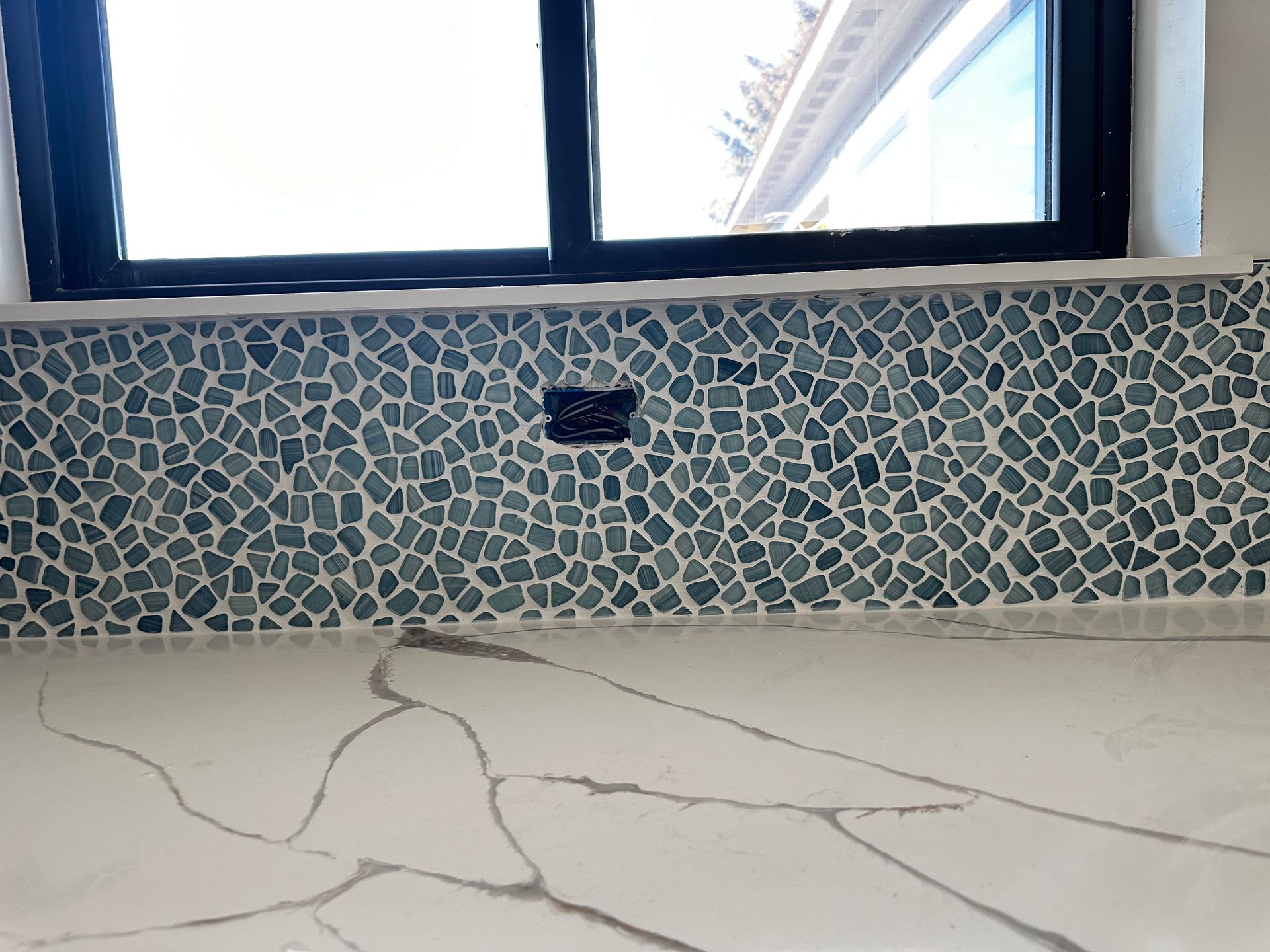 A kitchen counter with a mosaic tile backsplash and a window.