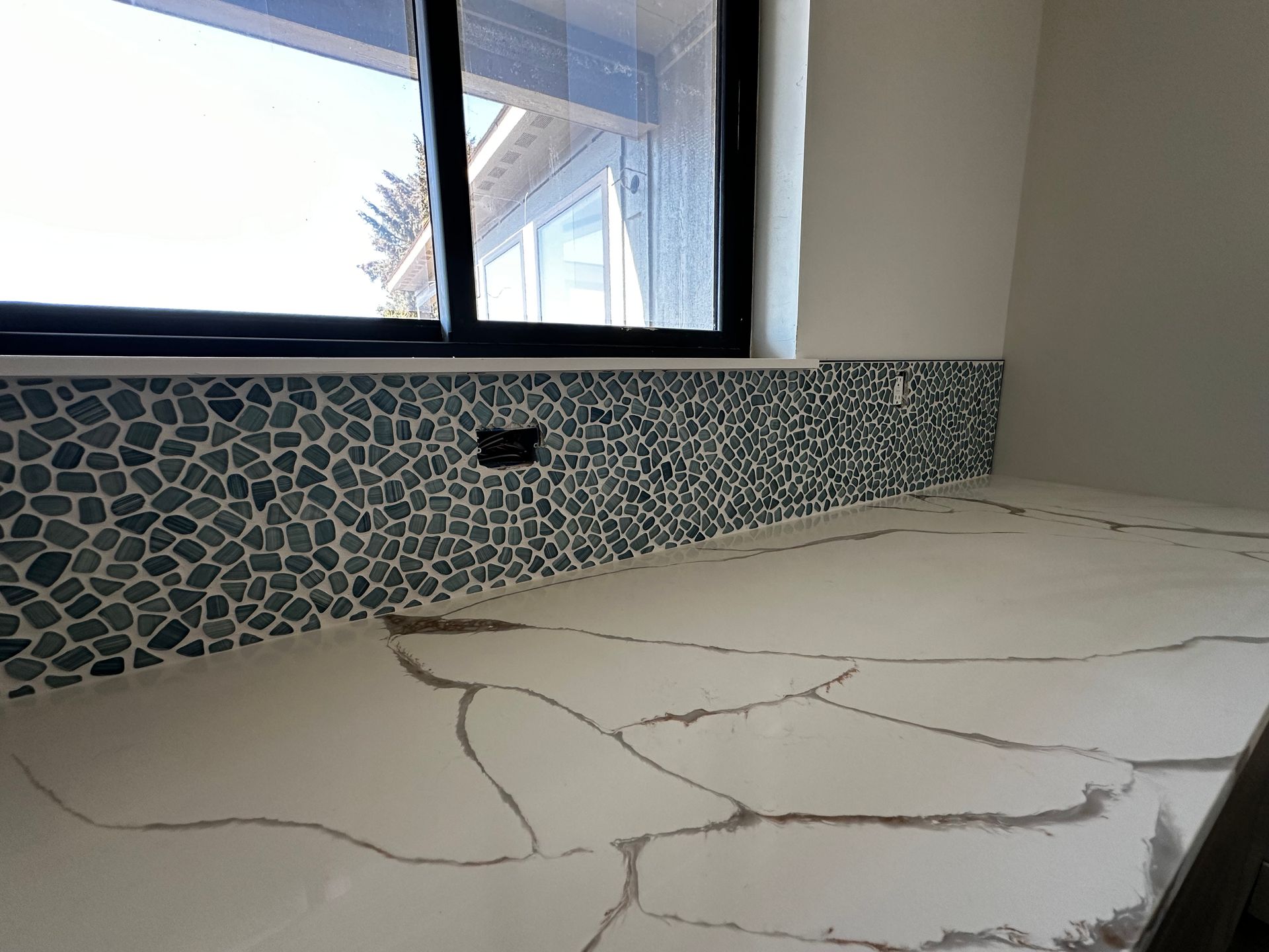 A kitchen counter with a window and a mosaic tile backsplash.