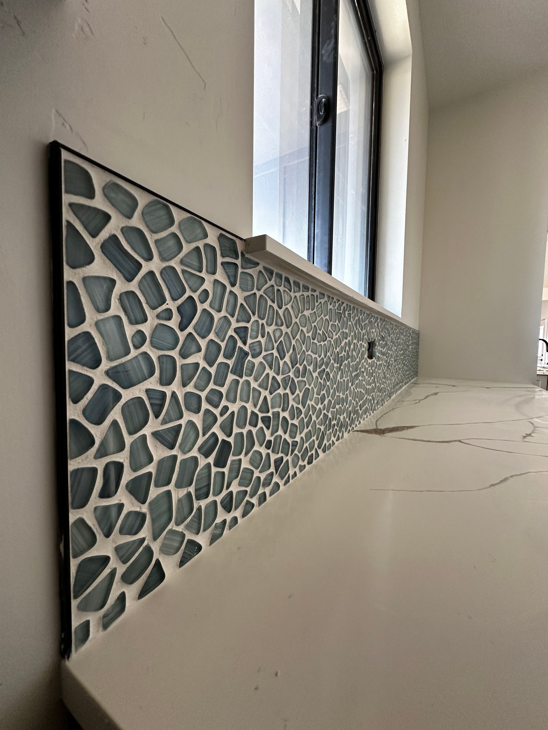 A kitchen counter with a mosaic tile backsplash and a window.