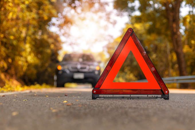 Orange Hazard  Road Sign placed on the road, with a car driving away from it in the background. 