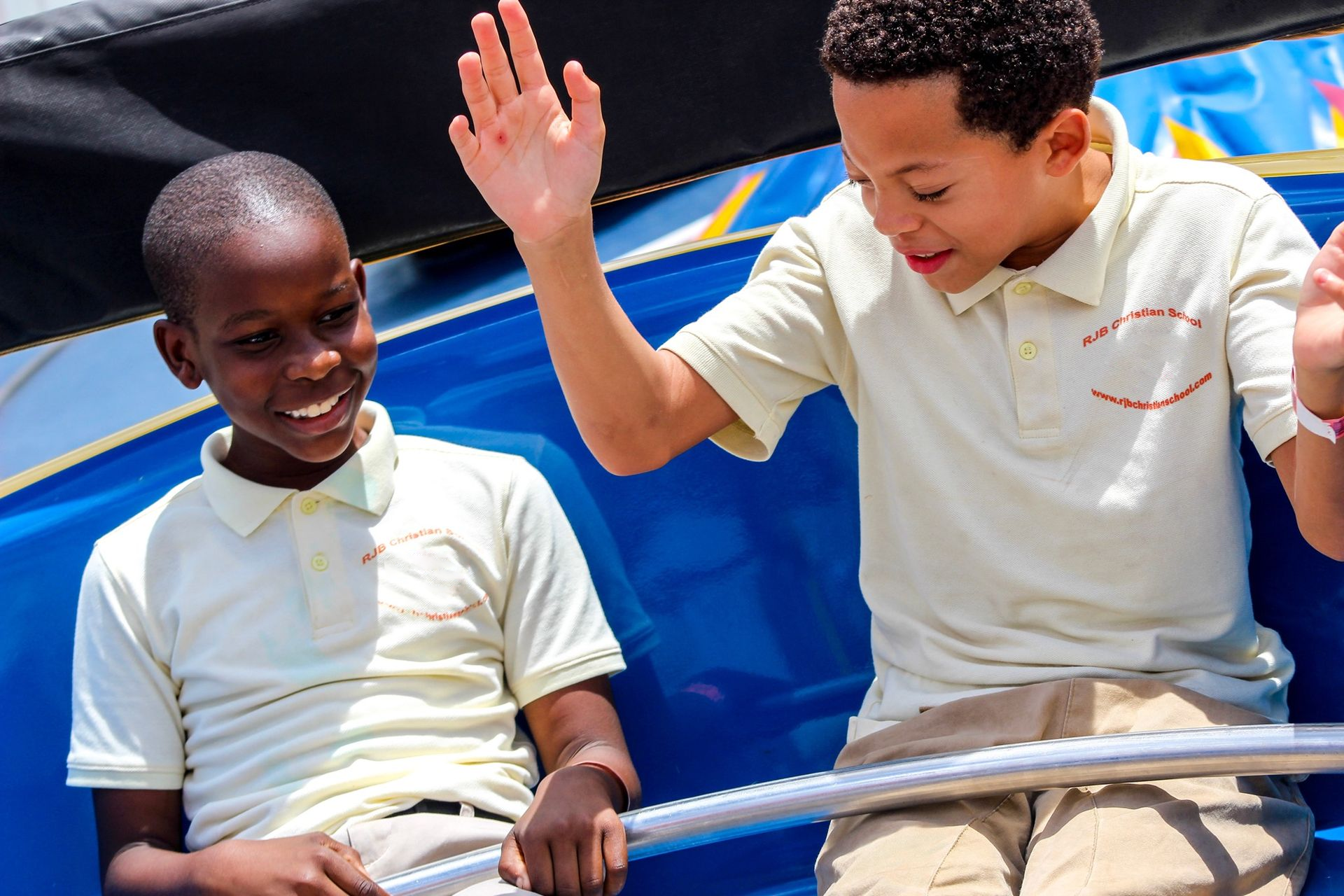 Two young boys are riding a roller coaster and one of them is giving the other a high five.