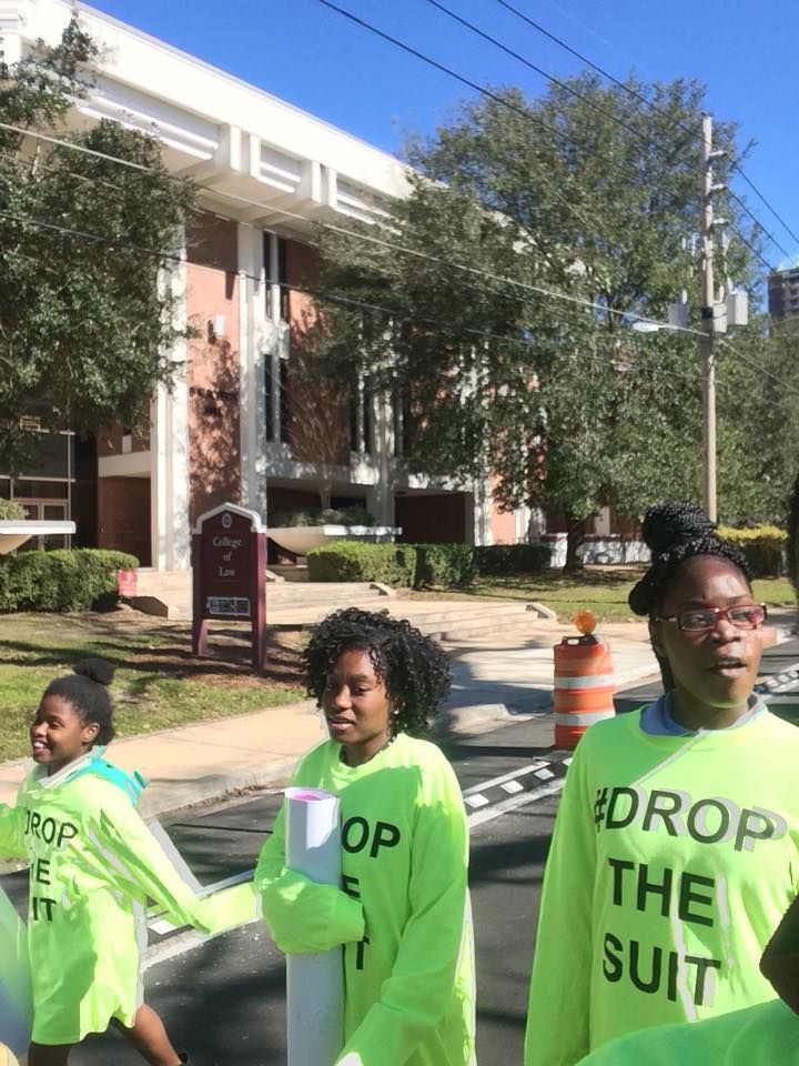 A group of people wearing neon yellow shirts that say drop the suit