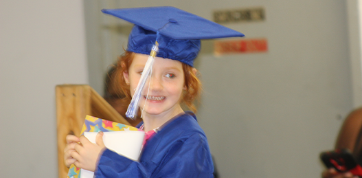 A young girl wearing a blue graduation cap and gown