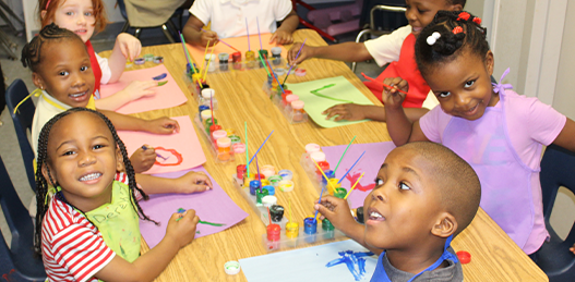 A group of children are sitting at a table painting.