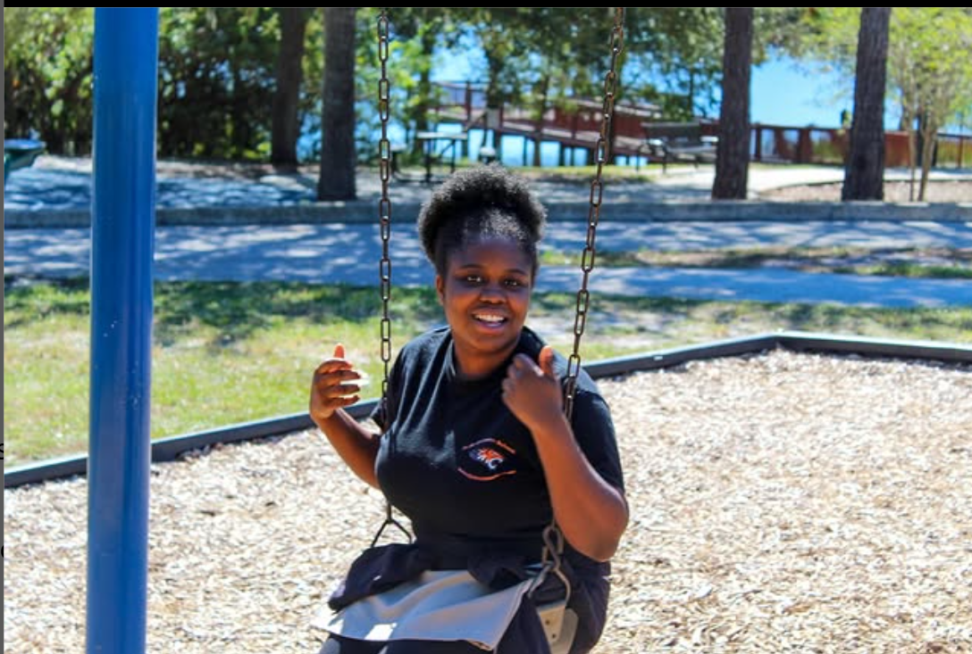 A woman is giving a thumbs up while sitting on a swing