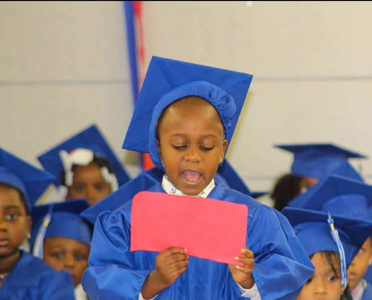 A young boy in a graduation cap and gown is holding a red piece of paper