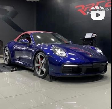 Um carro esporte azul está estacionado em frente a uma placa que diz desempenho na corrida