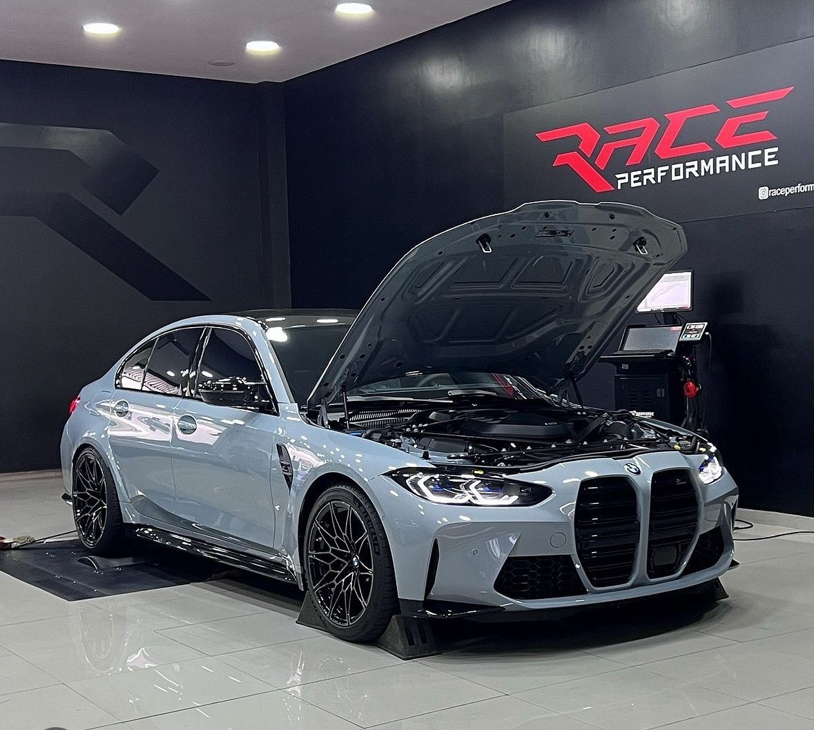 Um carro com o capô aberto está estacionado em uma garagem.