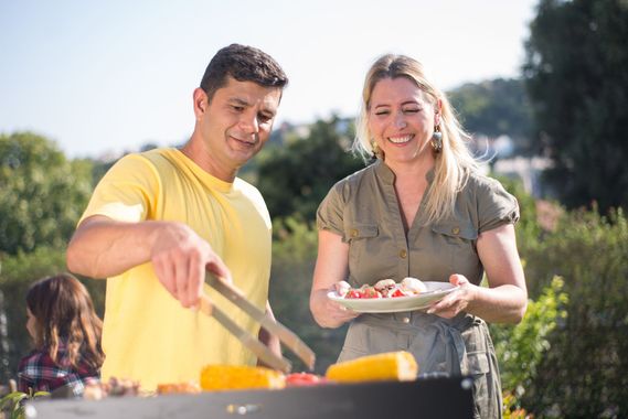Two people grilling outdoors, one stirring food on a barbecue while the other holds a plate of skewers