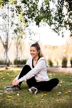 Woman sitting cross-legged on grass in a park, smiling under trees on a sunny day