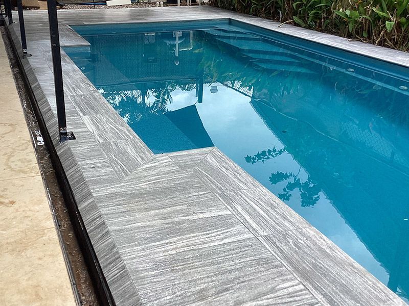 A Large Swimming Pool with A Wooden Deck Surrounding It — Paving in Darwin River, NT