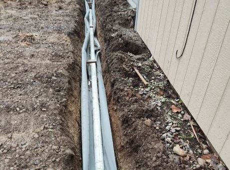 A pipe is being installed in a trench next to a house.