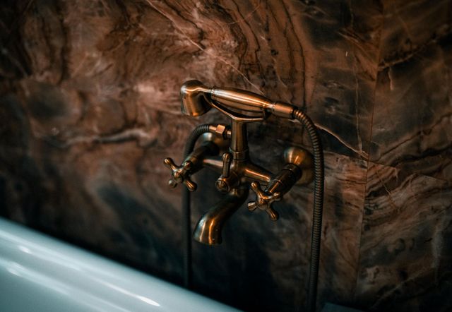 Bronze bathtub faucet against dark marbled tile wall