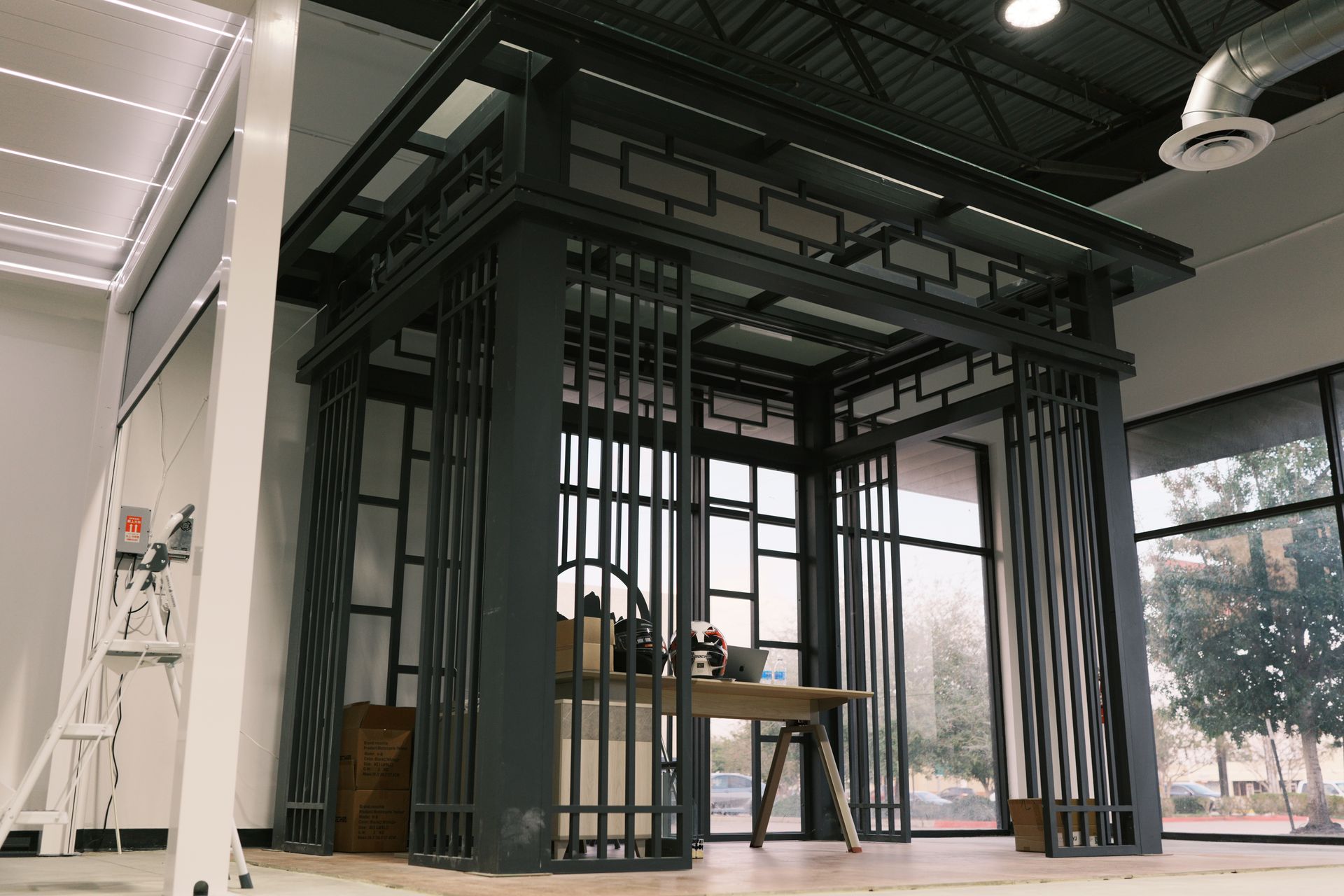 Modern black metal cage-like structure with a table inside an indoor room.