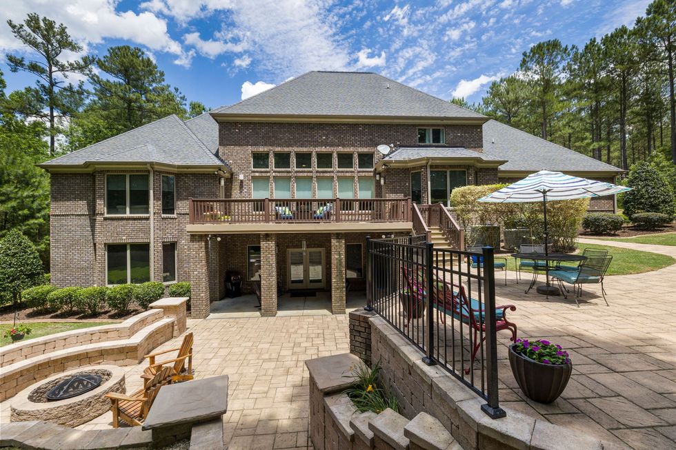 Backyard patio with stone house, fire pit, pool, and outdoor seating under umbrellas