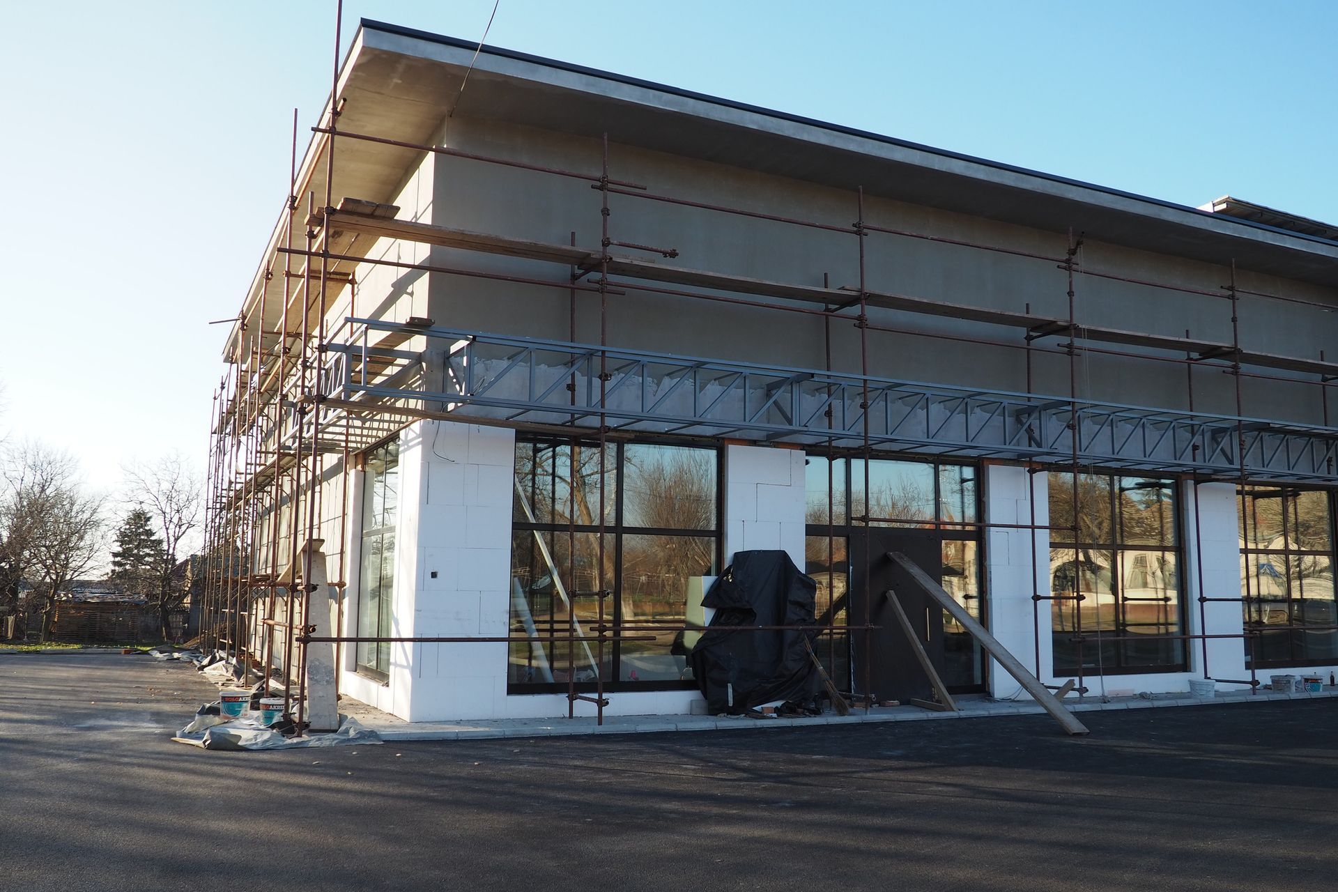 Building with scaffolding during renovation; windows, tan walls, dark roof, and asphalt parking lot.
