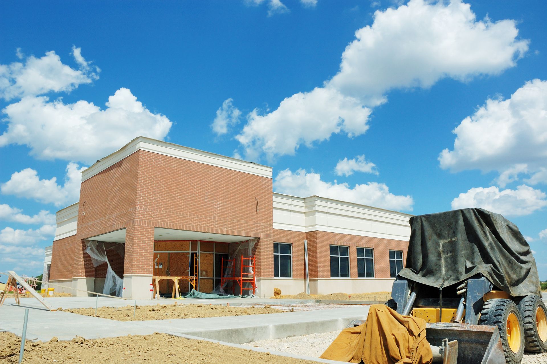 Building under construction, brick and concrete exterior against a blue sky, a bulldozer is present.