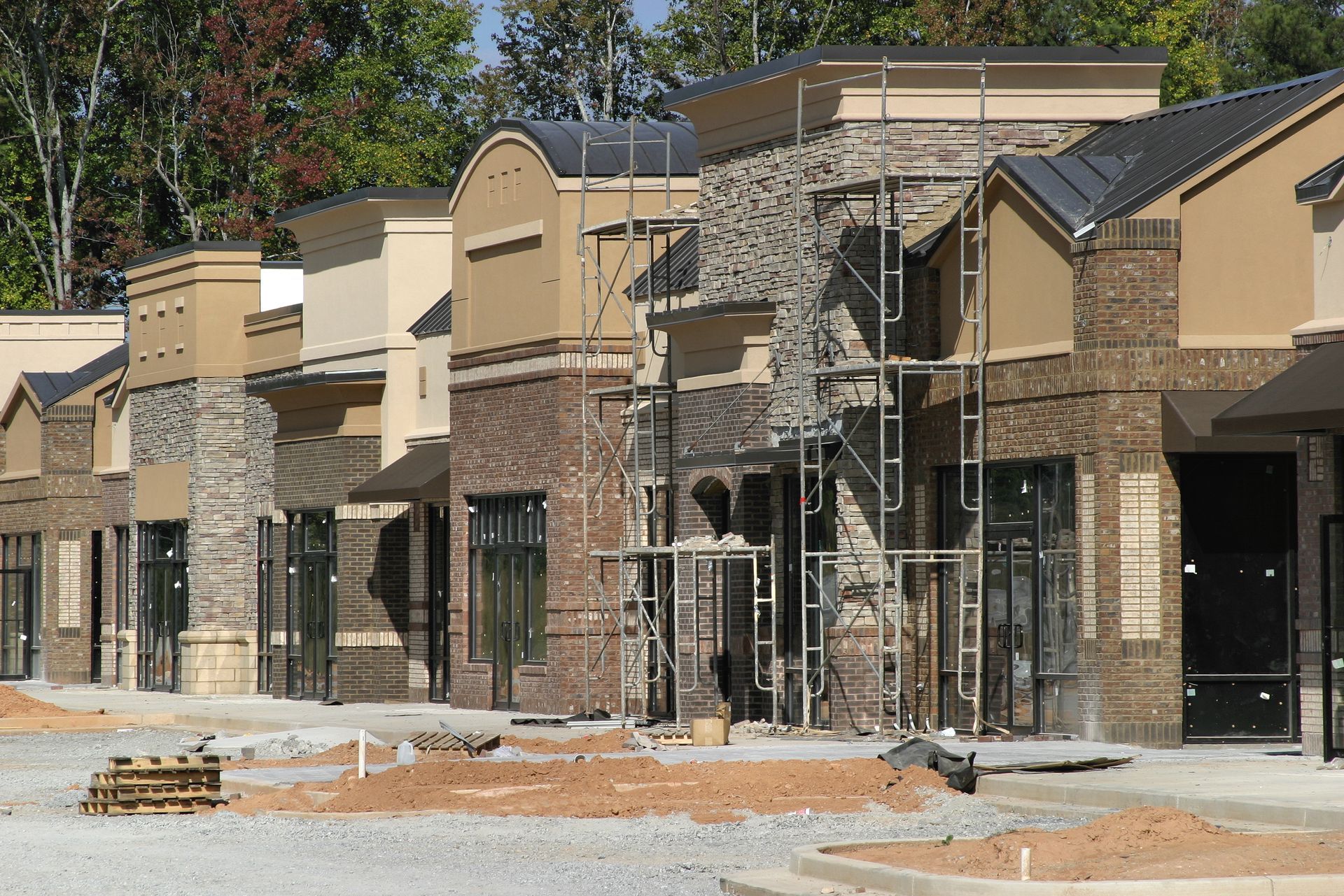 Row of unfinished commercial buildings with brick, beige, and stone facades; scaffolding present.