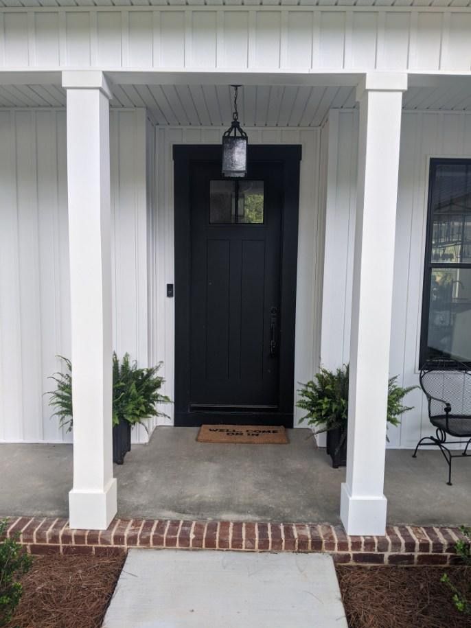 Black front door with a porch, white columns, and ferns in planters.