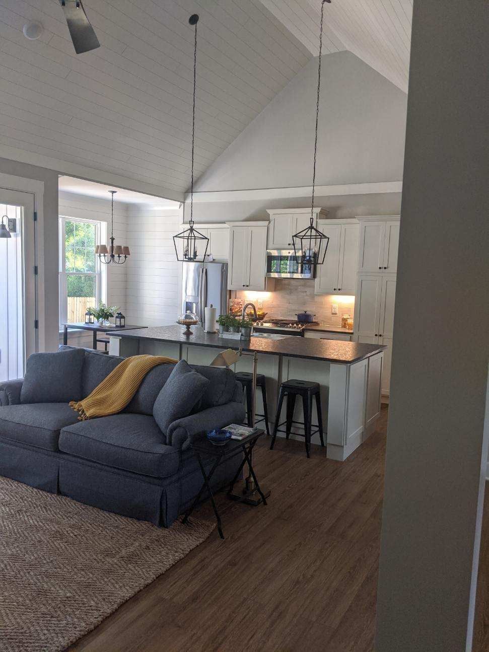 Living room with open kitchen. Gray couch, island with stools, two pendant lights.