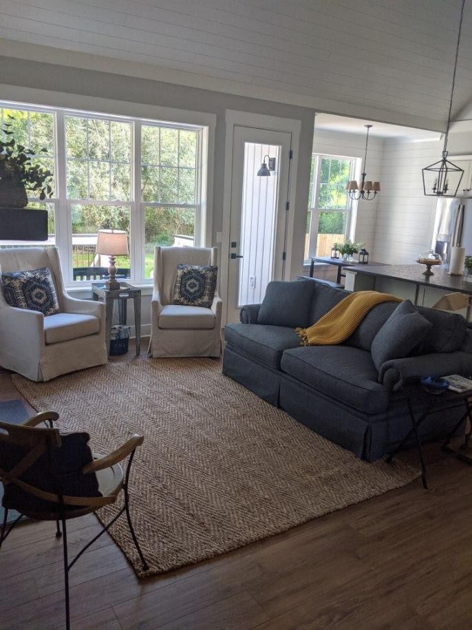 Living room with gray sofa, two armchairs, rug, and window with a view.
