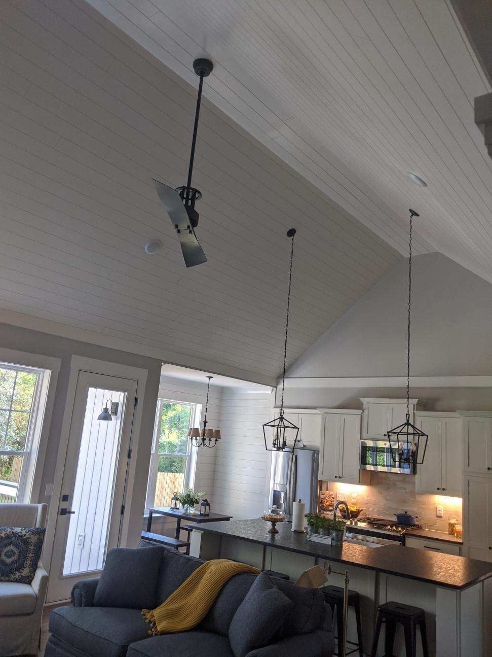 Living room with a gray couch, open kitchen with island, and hanging light fixtures.