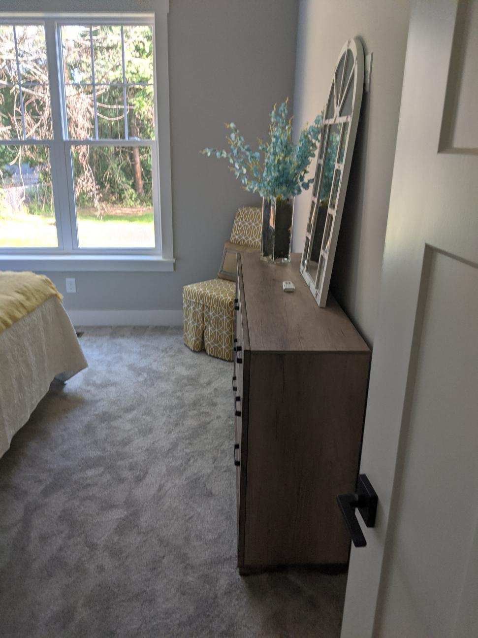 Bedroom with gray walls, carpet, dresser, window, and a decorative mirror.