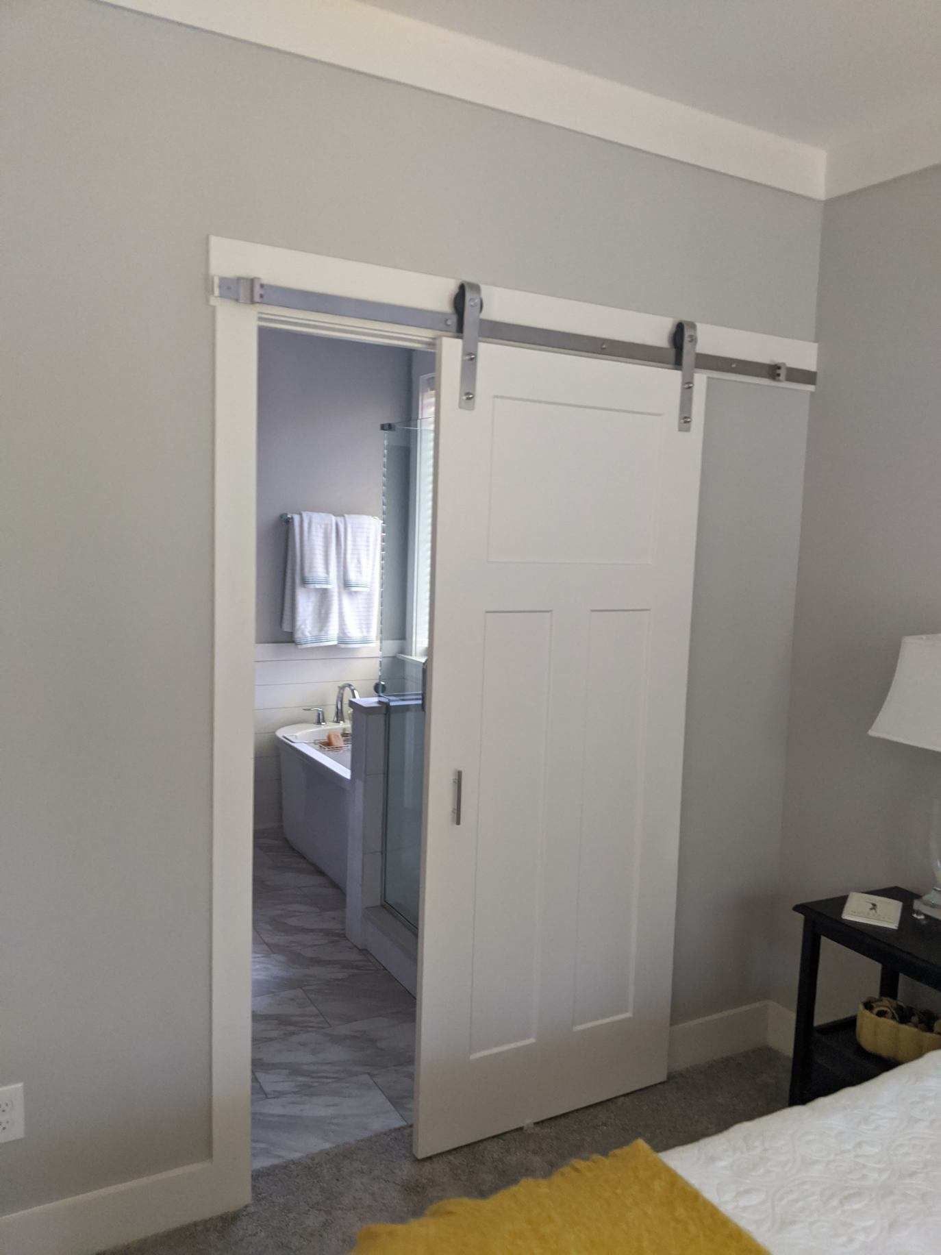 White barn door on a gray wall, open to reveal a bathroom.